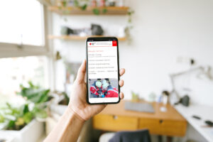 Auf dem Foto hält eine Frau ein Handy in der Hand, auf der die Website des DRK Ortsvereins Steinach zu sehen ist. Im Hintergrund sieht man verschwommen ein Arbeitszimmer.